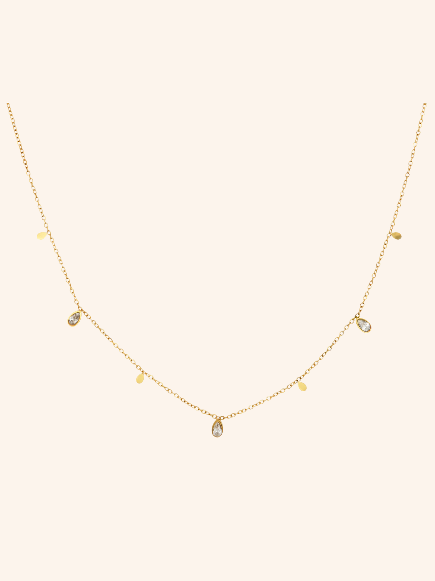 Glimmer Necklace i 18k PVD-guld med droppformade detaljer och zircon på ljus bakgrund