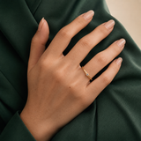 Dew Ring i 316 kirurgiskt stål och 18k PVD-guld, en tunn guldring med klar sten buren på hand mot mörkgrön textil.