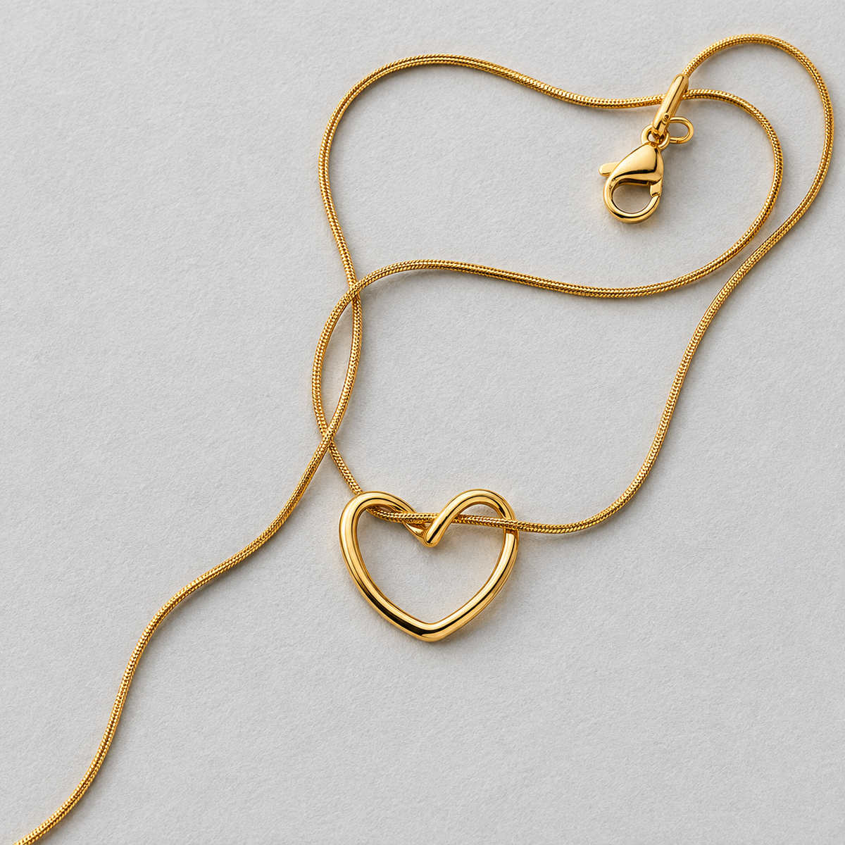 Echo Necklace i 316 kirurgiskt stål och 18k PVD-guld, detaljbild på guldfärgat halsband med öppet hjärthänge mot ljus neutral bakgrund.