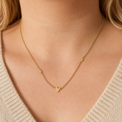 Ember Necklace i 316 kirurgiskt stål och 18k PVD-guld, ett guldfärgat halsband med små hjärtdetaljer buret på halsen.