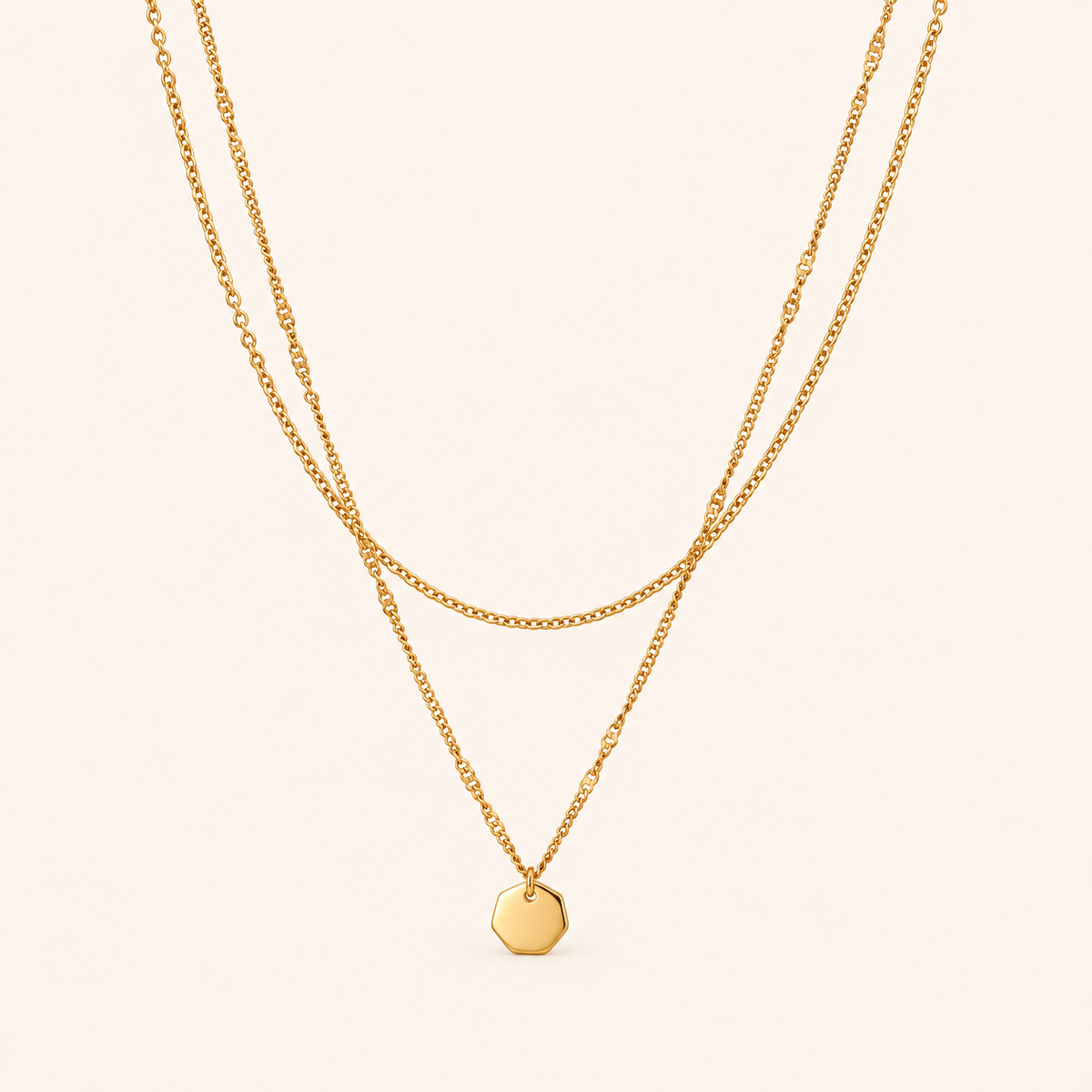 Facet Layer Necklace i 18k PVD-guld med dubbla kedjor och litet oktagonformat hänge på ljus bakgrund.