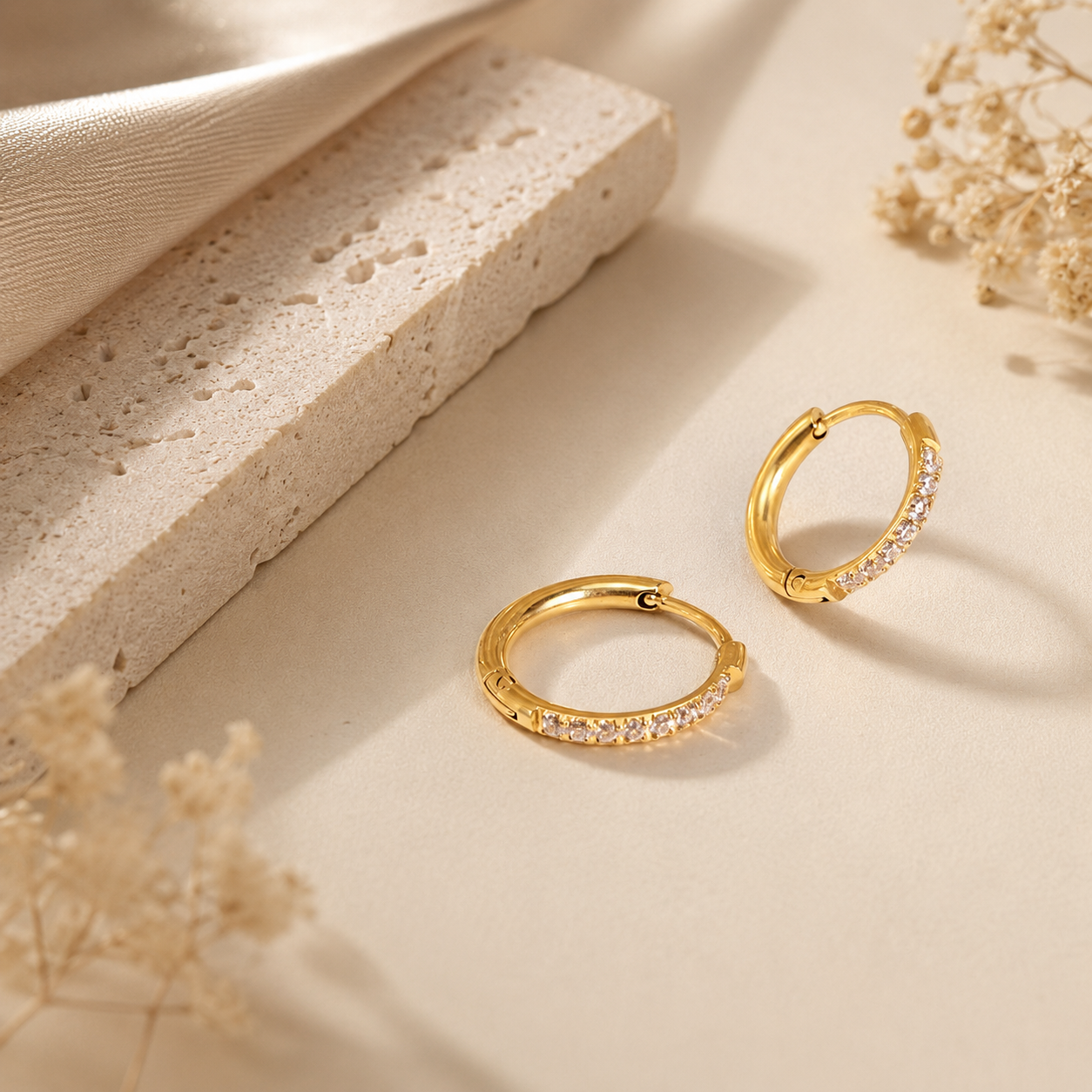 Frost Hoop örhängen i 316 kirurgiskt stål och 18k PVD-guld, med klara stenar på varm beige bakgrund.
