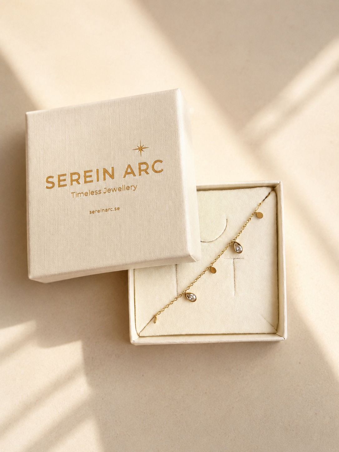 Glimmer Bracelet i 316 kirurgiskt stål och 18k PVD-guld, placerat i en Serein Arc smyckesask mot varm neutral bakgrund.