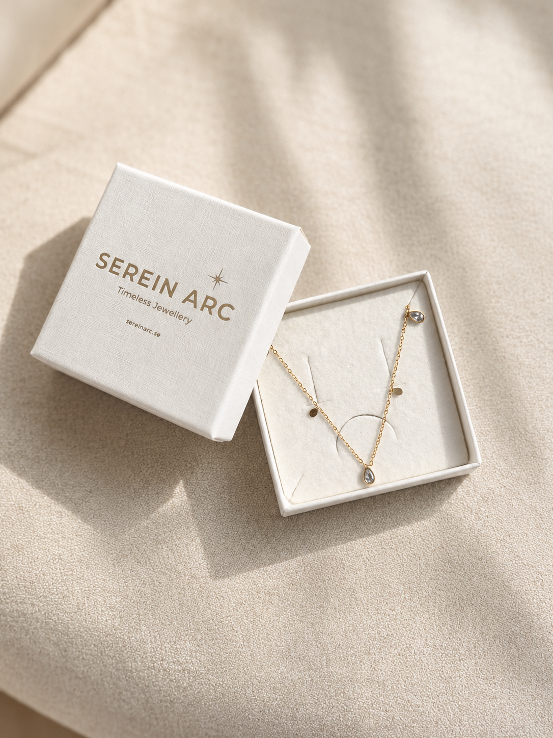 Glimmer Necklace i 316 kirurgiskt stål och 18k PVD-guld, placerat i en Serein Arc smyckesask mot varm neutral bakgrund.