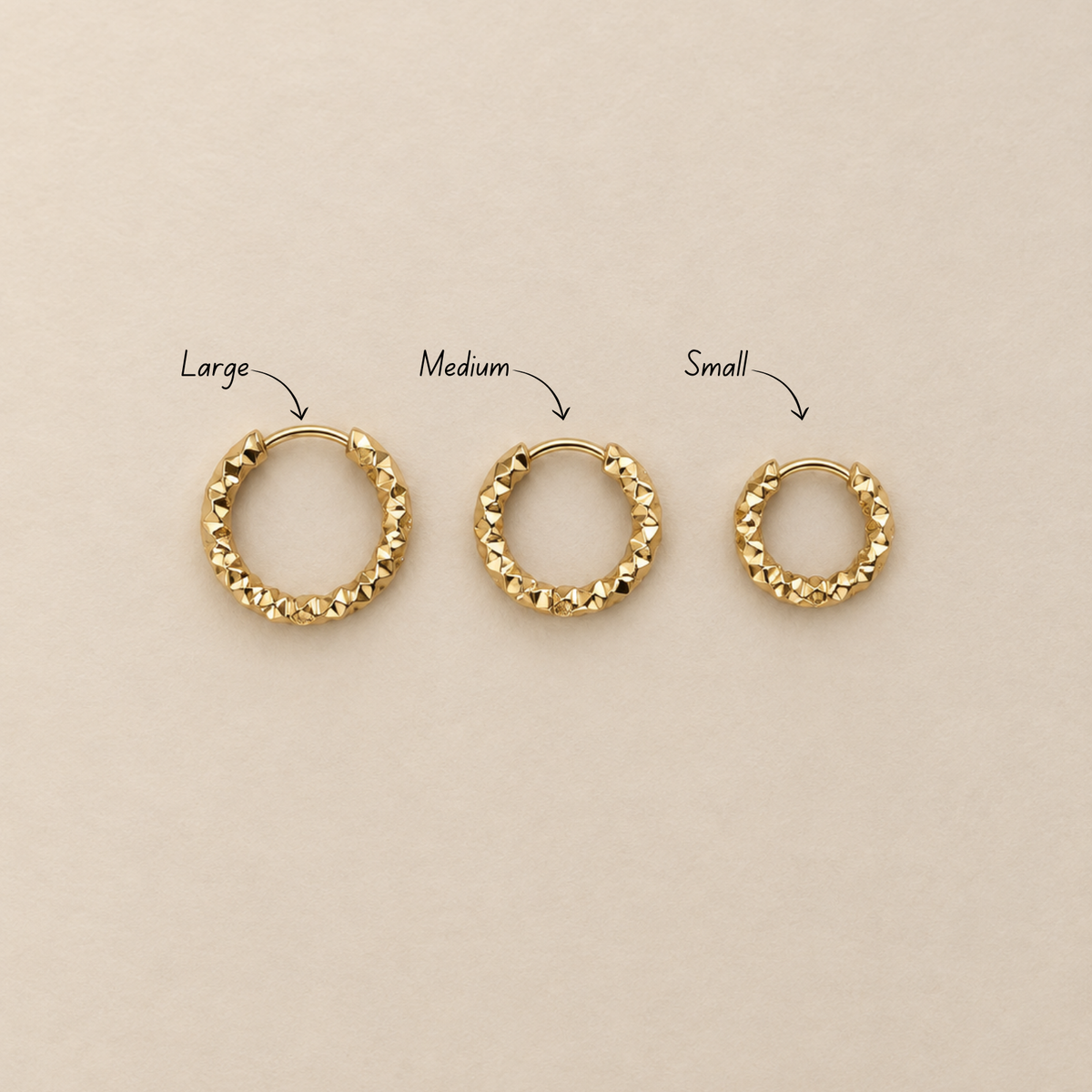 Grain Hoop örhängen i guld visade i small, medium och large på ljus bakgrund.