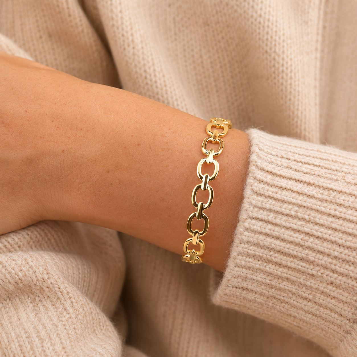 Loop Bracelet i 316 kirurgiskt stål och 18k PVD-guld, ett guldfärgat kedjearmband buret på handleden mot beige stickad textil.
