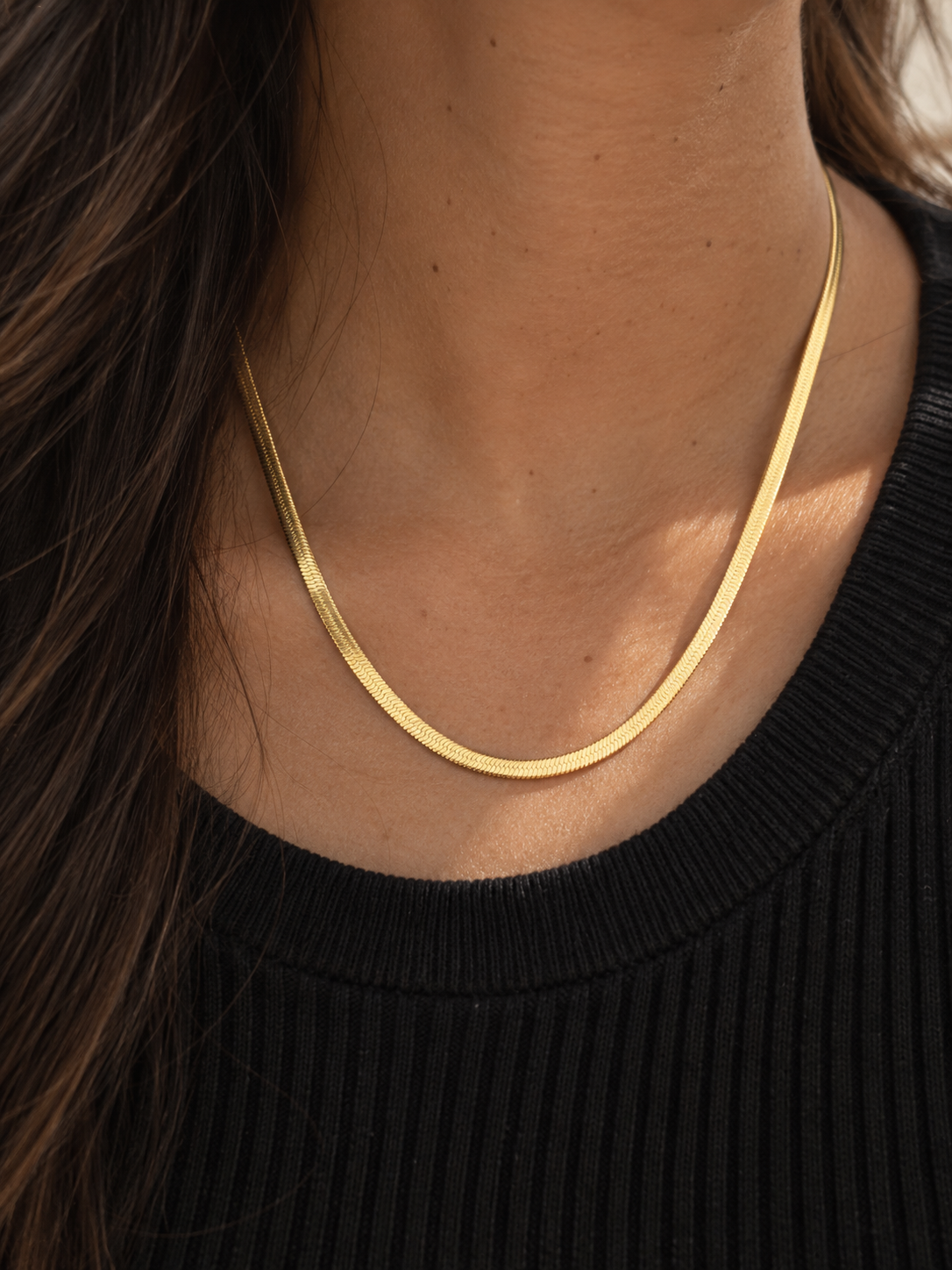 Lune Necklace 3mm i guld buren på halsen med svart topp i varmt dagsljus.