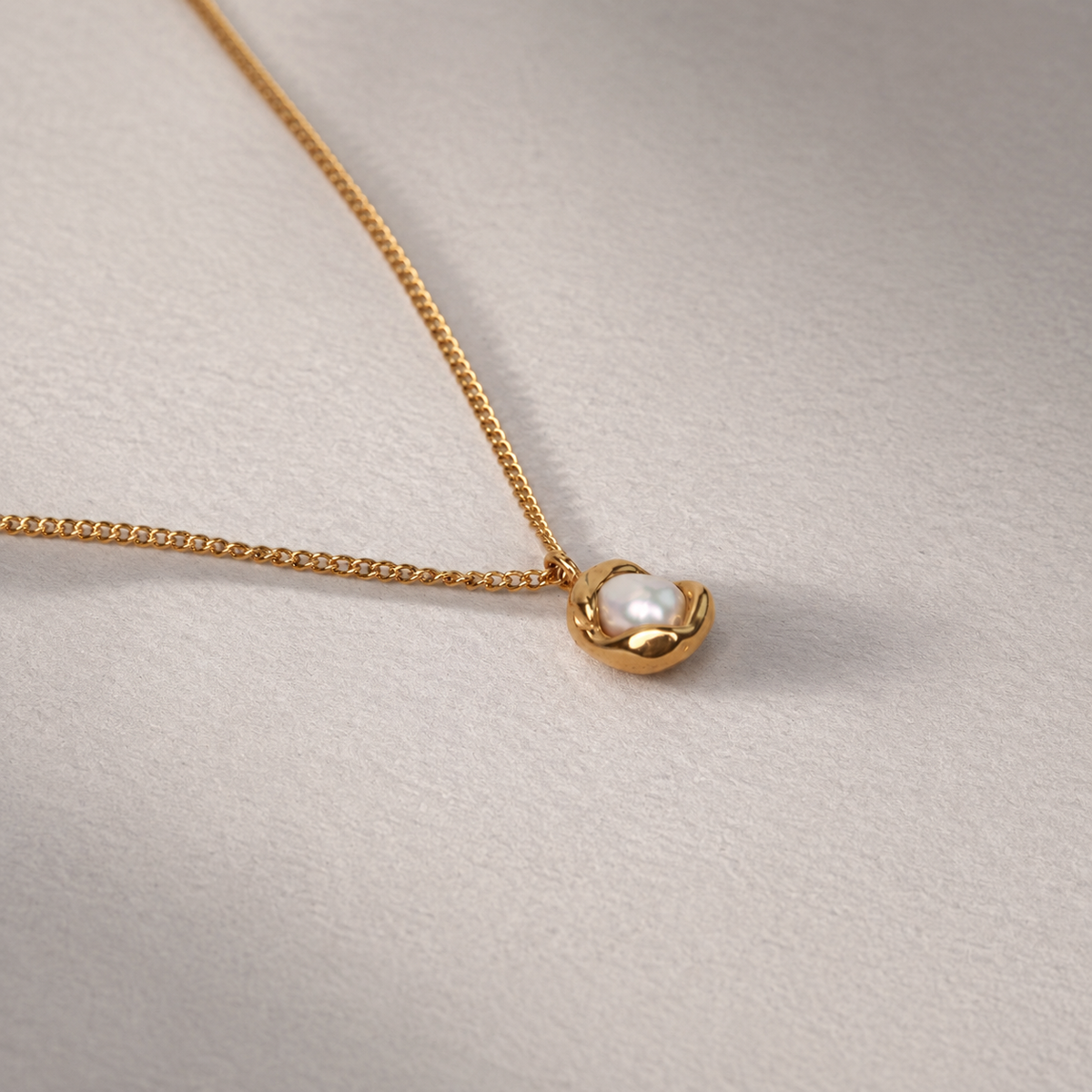 Oyster Necklace i 316 kirurgiskt stål och 18k PVD-guld, detaljbild på guldfärgat hänge med pärla mot ljus neutral bakgrund.