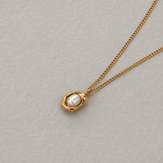 Oyster Necklace i 316 kirurgiskt stål och 18k PVD-guld, guldfärgat halsband med rundad pärldetalj mot ljus neutral bakgrund.