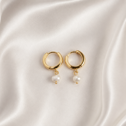 Pearl Drop i 316 kirurgiskt stål och 18k PVD-guld, huggie-örhängen med pärldetaljer på ljus satinbakgrund.