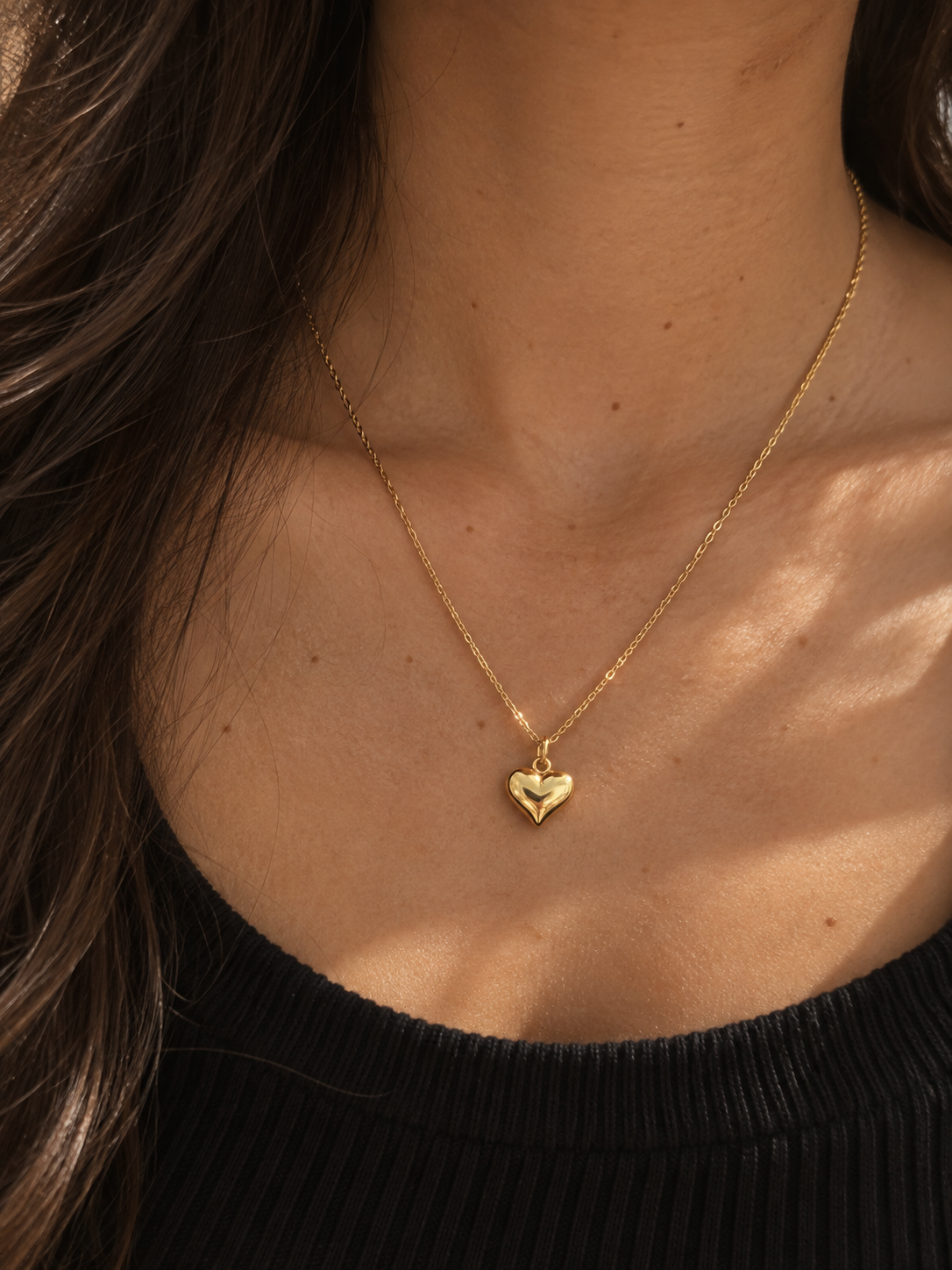 Pulse Necklace i guld med hjärtformad berlock buren på halsen i varmt dagsljus.