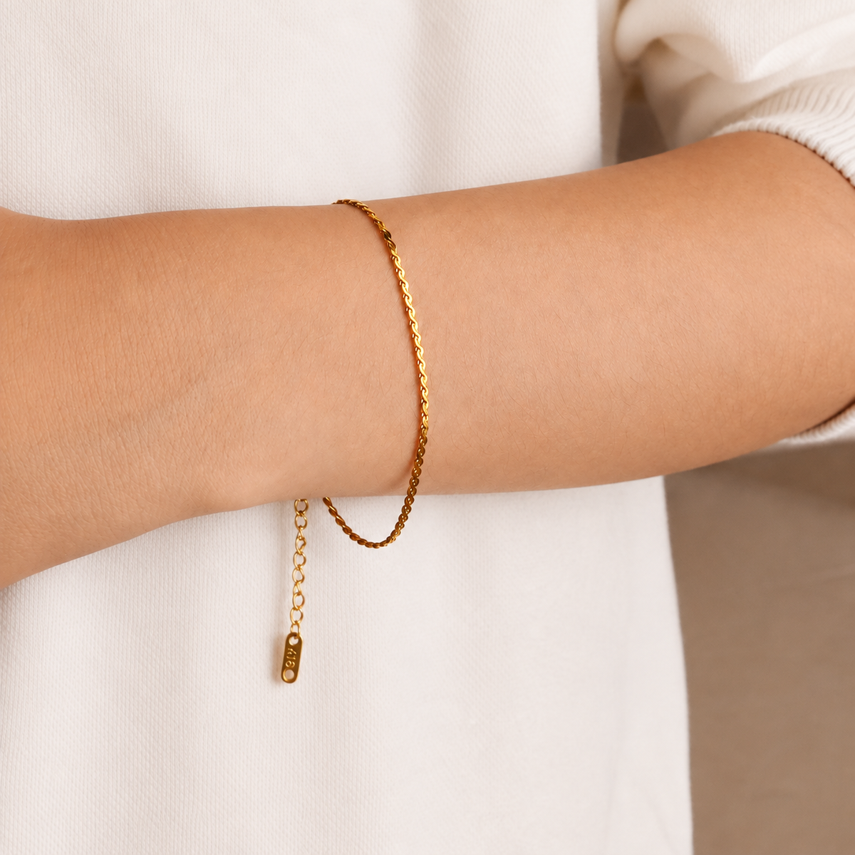 Ripple Bracelet, ett tunt guldfärgat armband stylat på handleden med förlängningskedja synlig mot en vit tröja.