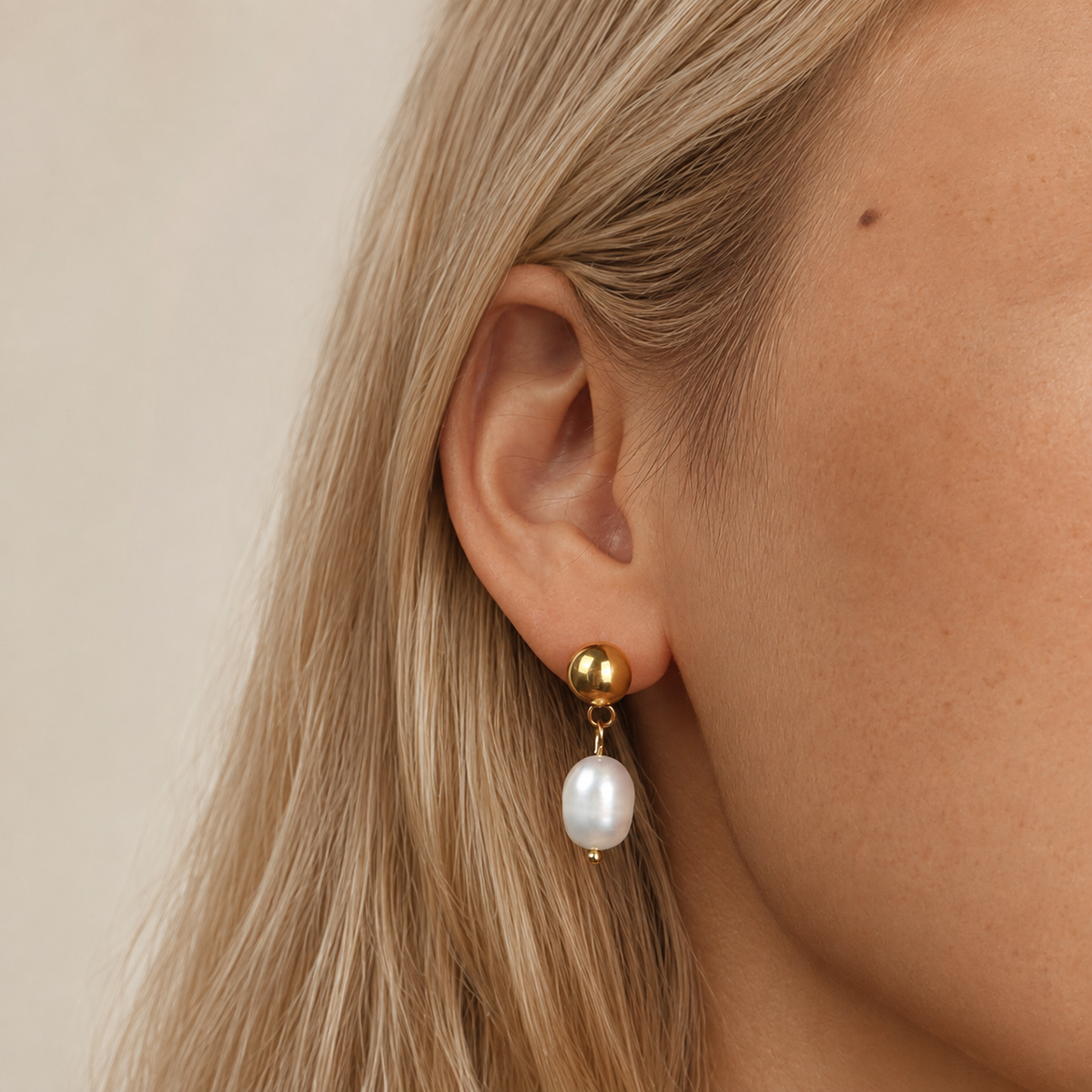 Satin Pearl Drop i 316 kirurgiskt stål och 18k PVD-guld, ett pärlörhänge med rund guldfärgad stud buret i örat.