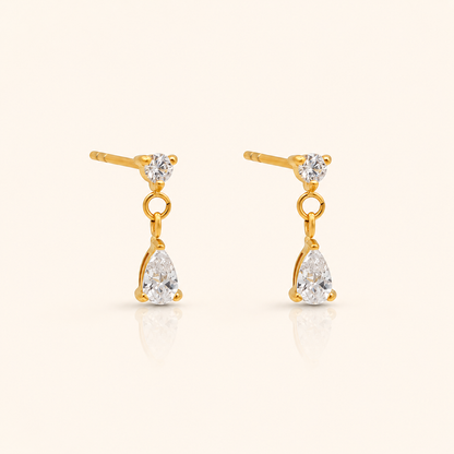 Cascade Stud örhängen i 18k PVD-guld med rund zircon och hängande droppformad zircon på ljus bakgrund
