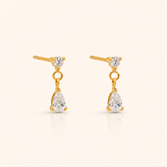 Cascade Stud örhängen i 18k PVD-guld med rund zircon och hängande droppformad zircon på ljus bakgrund