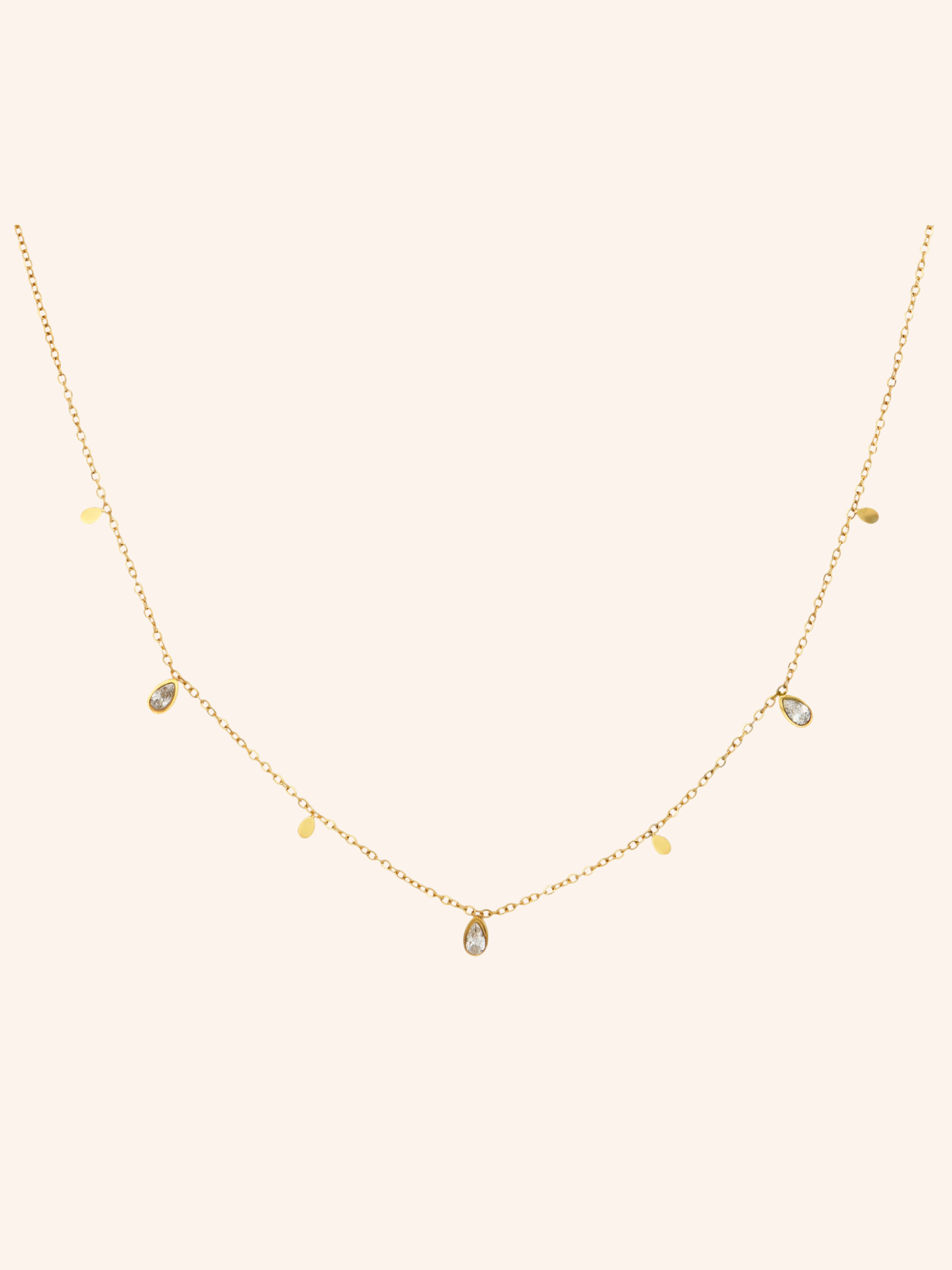 Glimmer Necklace i 18k PVD-guld med droppformade detaljer och zircon på ljus bakgrund
