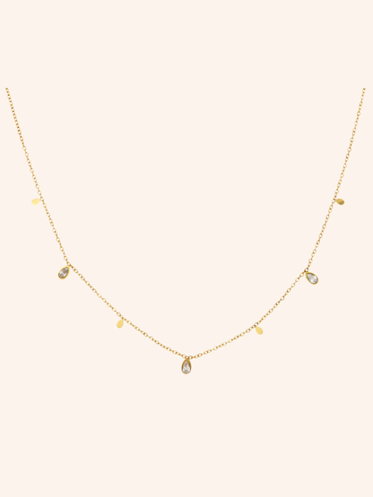 Glimmer Necklace i 18k PVD-guld med droppformade detaljer och zircon på ljus bakgrund