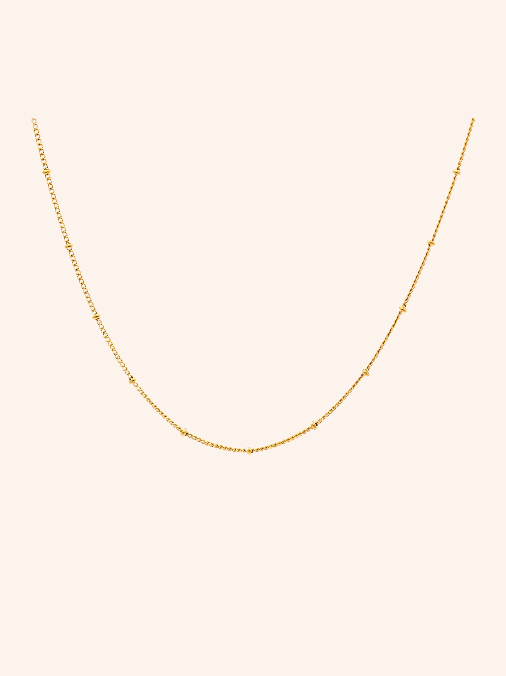 Tether Necklace i 18k PVD-guld med små detaljer längs kedjan på ljus bakgrund