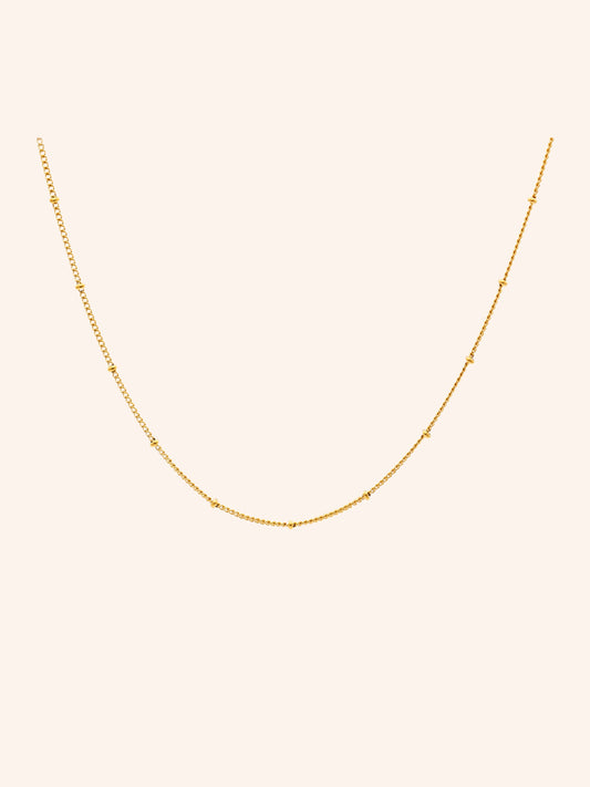 Tether Necklace i 18k PVD-guld med små detaljer längs kedjan på ljus bakgrund