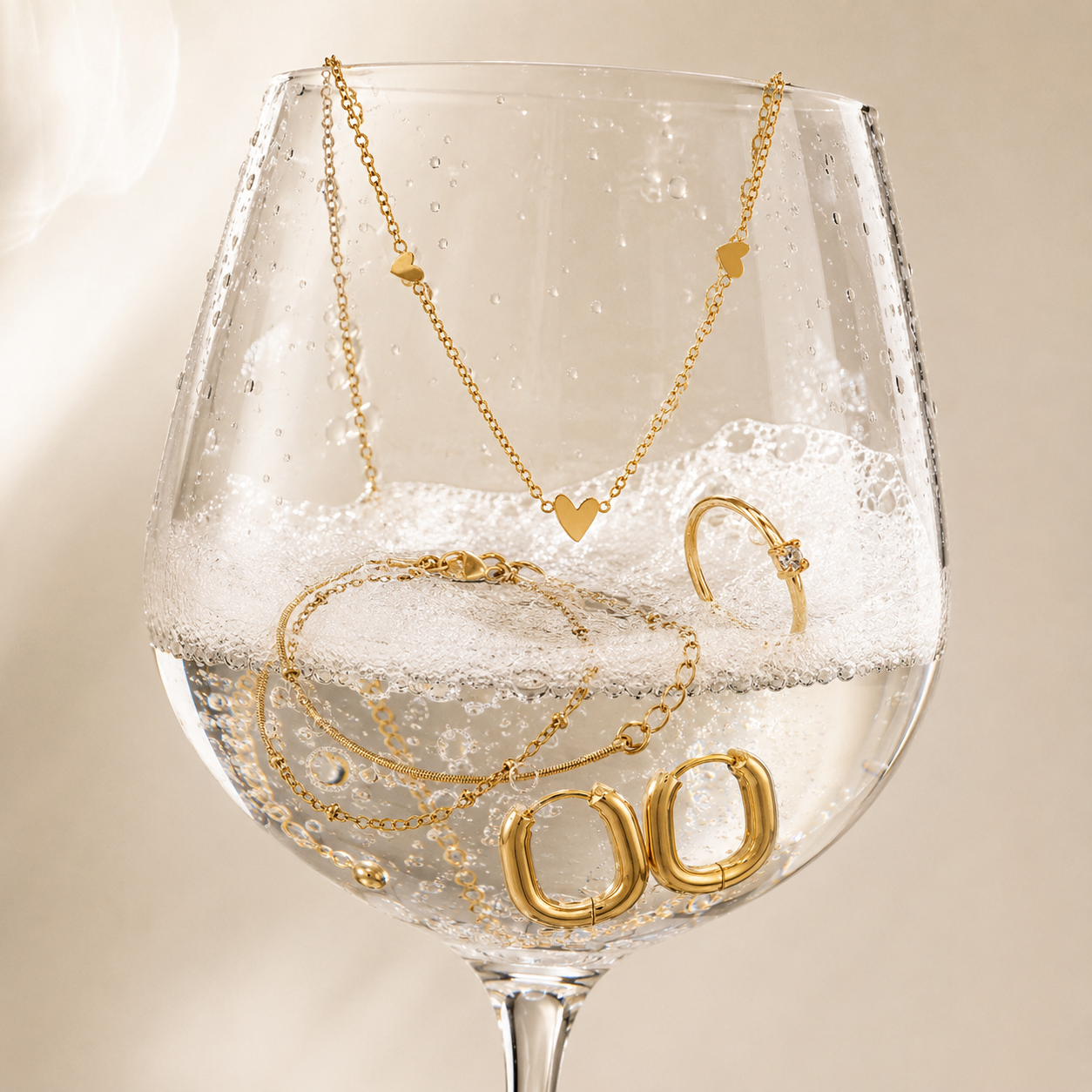 Vattentåliga smycken i 316 kirurgiskt stål och 18k PVD-guld från Serein Arc, med halsband, armband, ring och hoops i ett glas med vatten.