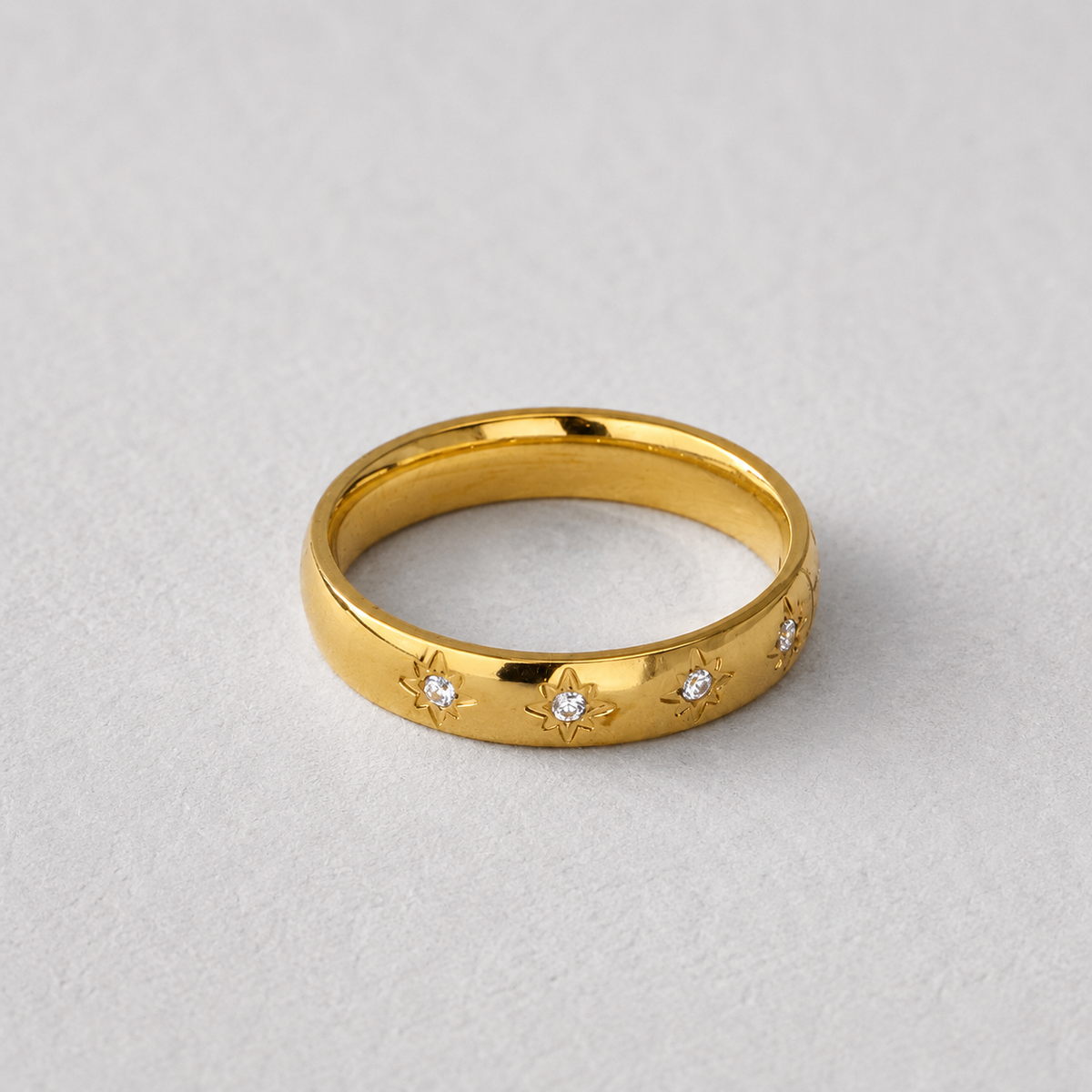 Sol Ring, guldfärgad ring med små klara stenar infattade i stjärnformade detaljer, fotograferad mot ljus neutral bakgrund.