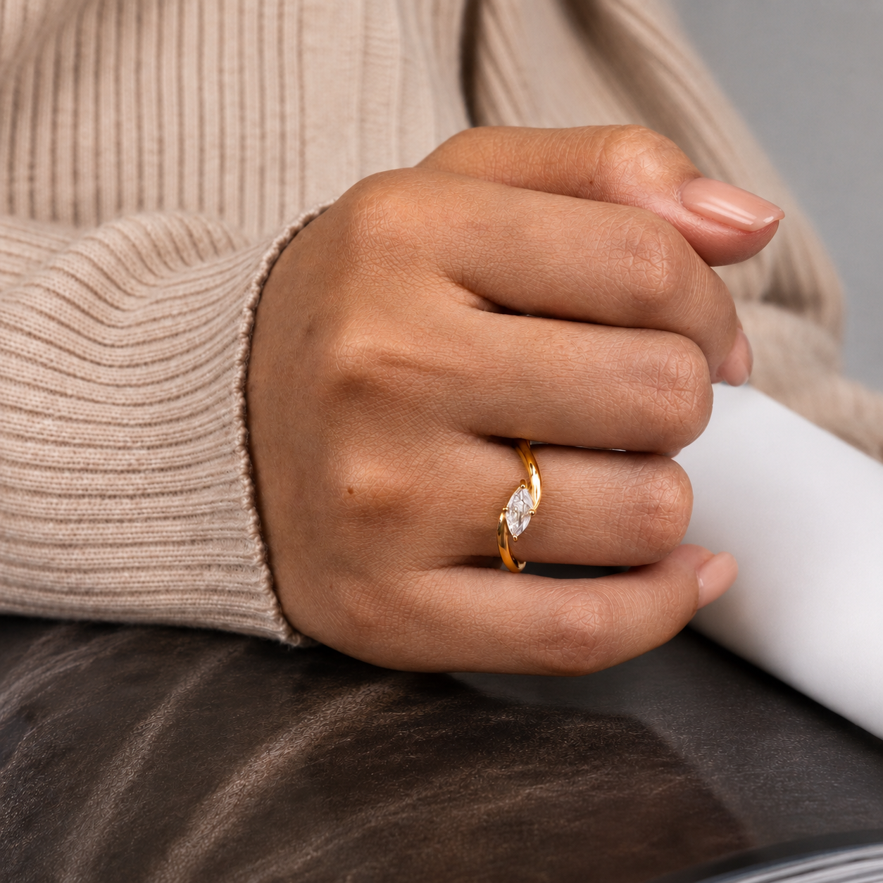 Sway Ring, en guldfärgad ring med en marquiseformad klar sten, buren på handen tillsammans med en beige stickad tröja.