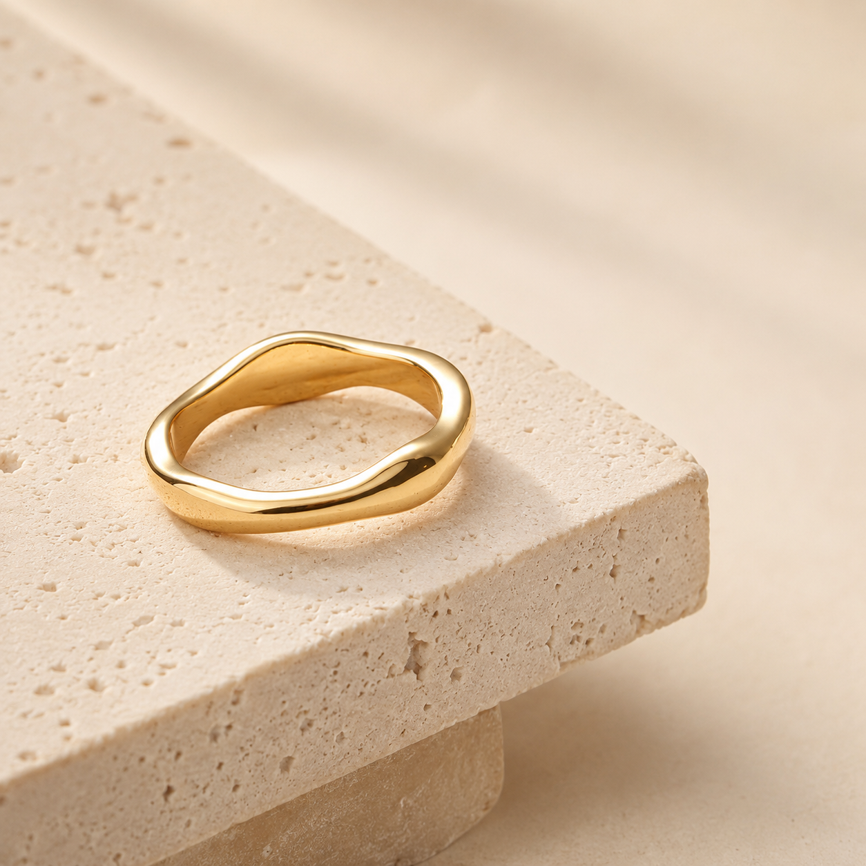 Trace Ring i 316 kirurgiskt stål och 18k PVD-guld, en mjukt formad guldring på varm beige stenbakgrund.