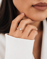 Twin Gleam Ring i 316 kirurgiskt stål och 18k PVD-guld, en öppen guldring med två klara stenar buren på hand mot svart stickad textil.